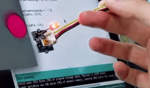A hand holding a small machine in front of computer code